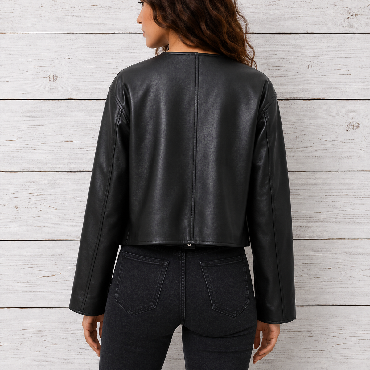 A woman shown from the back wearing a cropped black faux-leather jacket and dark jeans
