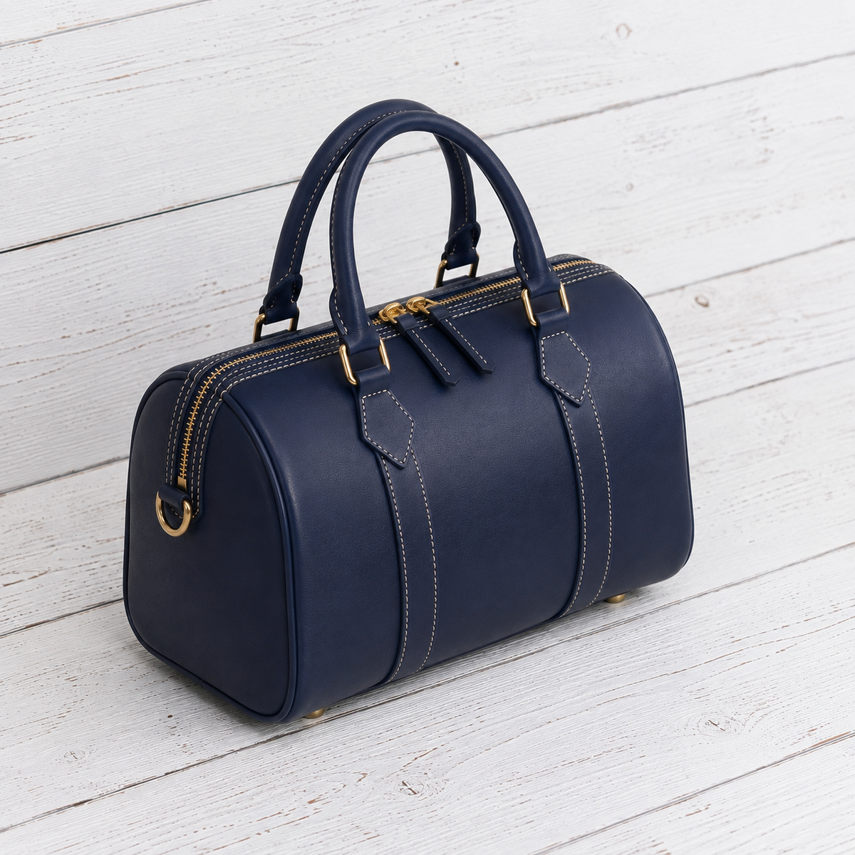 A navy blue leather travel bag with gold-tone hardware, featuring dual top handles, a zippered top closure, and decorative contrast stitching