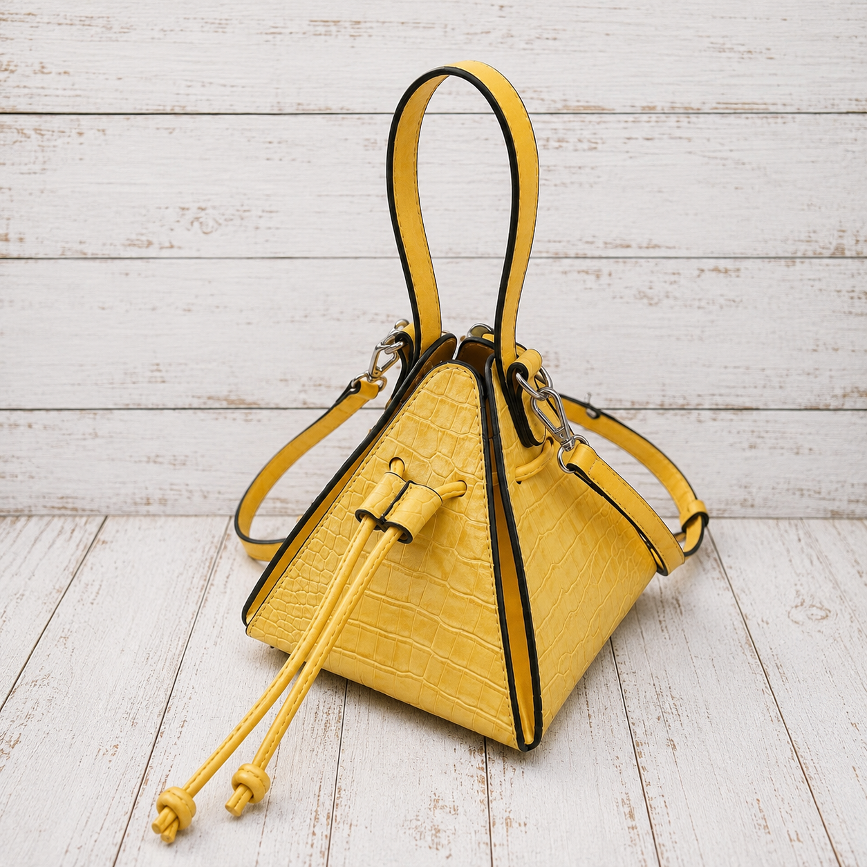 A bright yellow crocodile-embossed leather handbag with black trim and a matching drawstring detail
