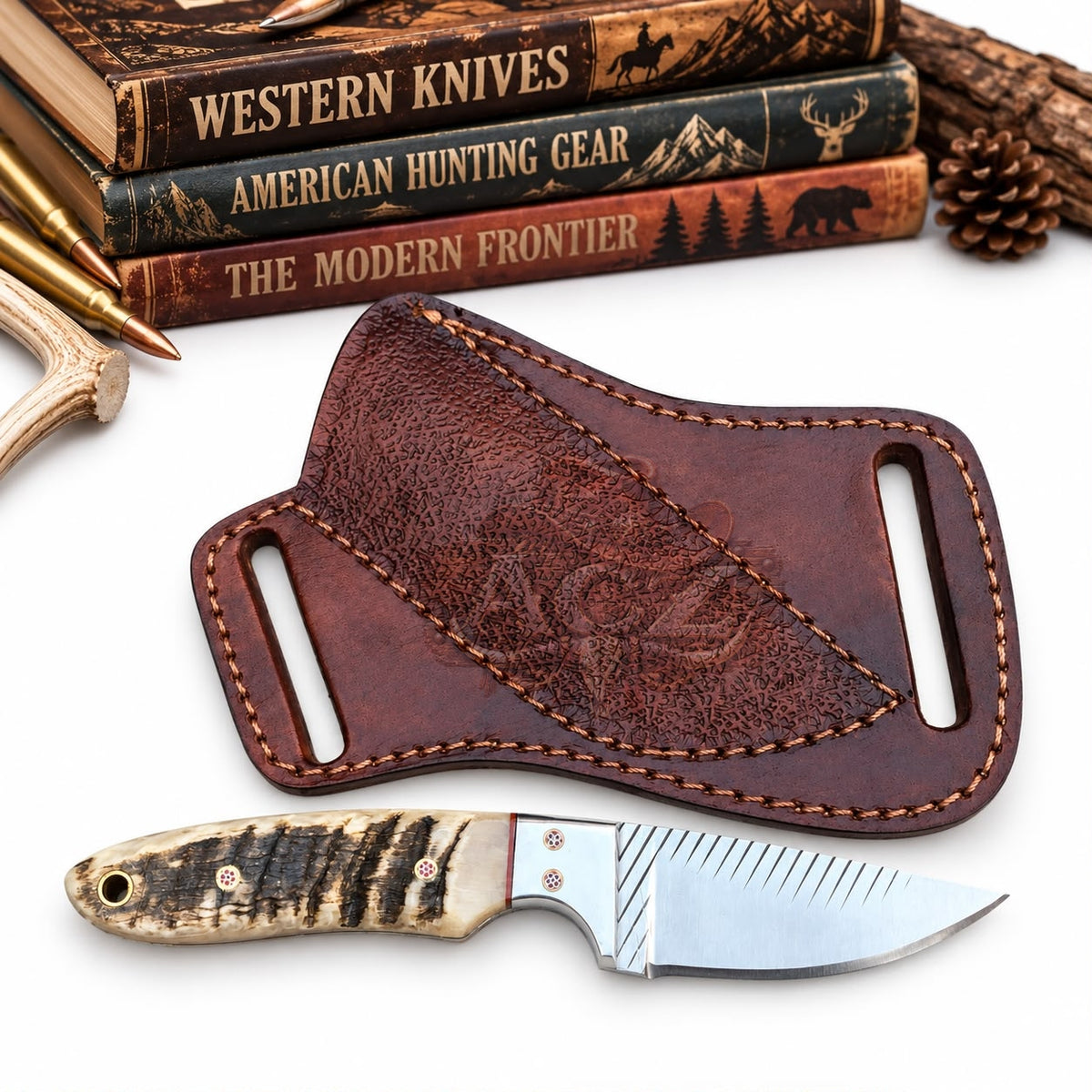 A leather knife sheath and a fixed-blade knife displayed on a white background with rustic props including books, a bullet, antler, and pine cone.