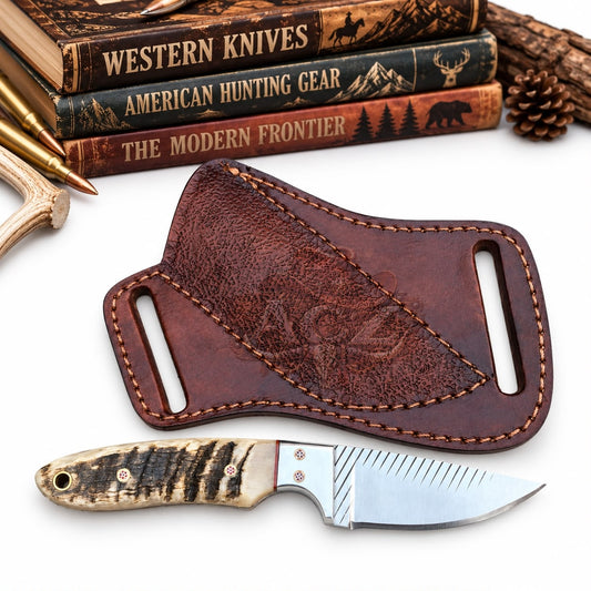 A leather knife sheath and a fixed-blade knife displayed on a white background with rustic props including books, a bullet, antler, and pine cone.