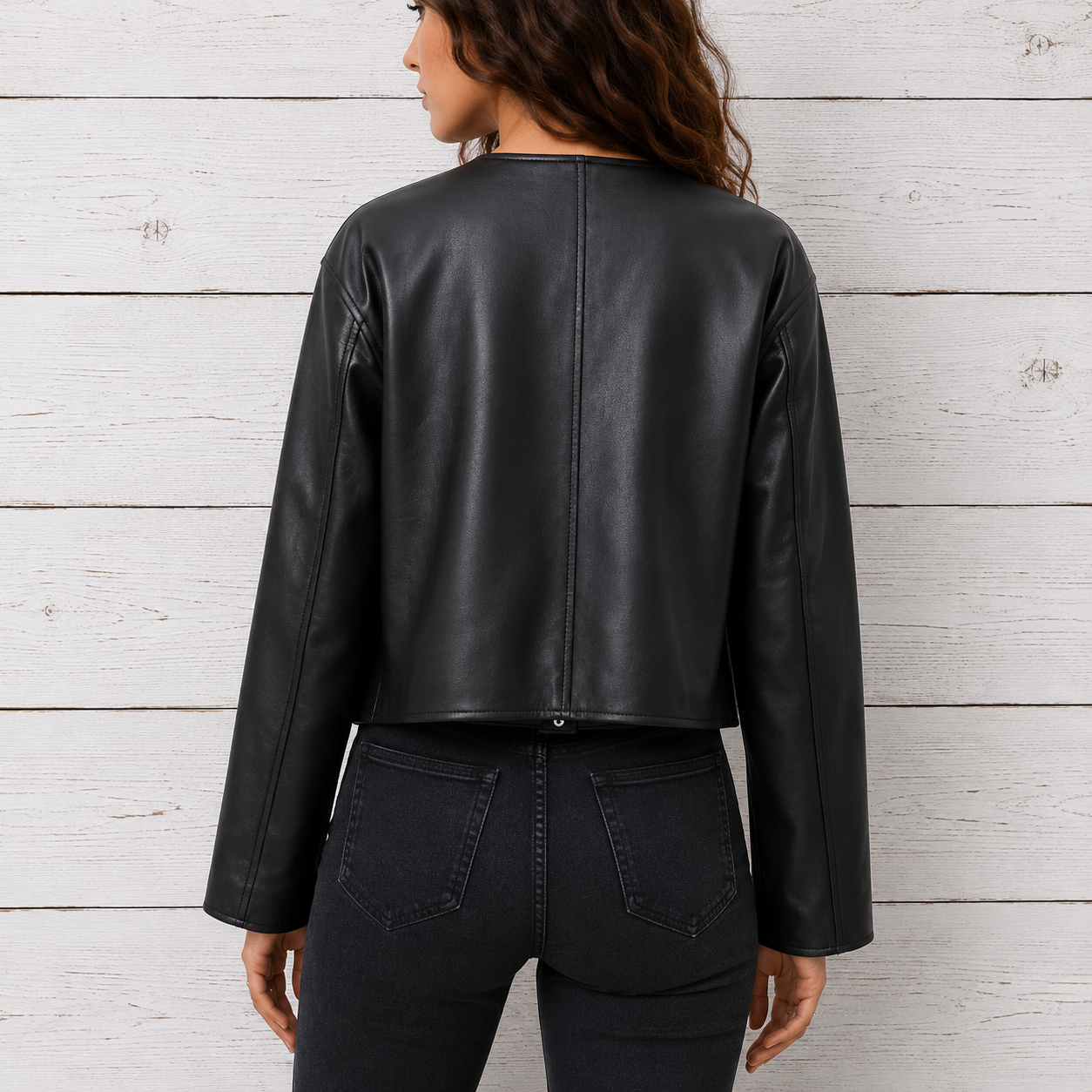 A woman shown from the back wearing a cropped black faux-leather jacket and dark jeans