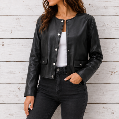 A woman wearing a black faux-leather cropped jacket with silver snap buttons, styled over a white top and black jeans