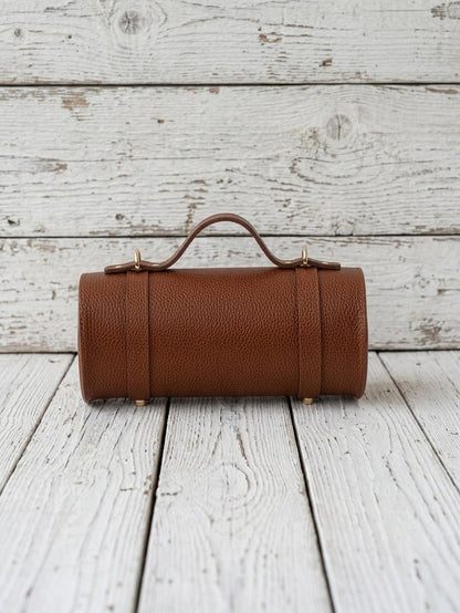 A brown textured leather cylindrical handbag with a top handle and gold-tone hardware