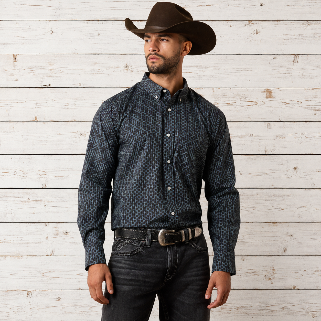 A man wearing a dark navy long-sleeve button-down shirt with a small white geometric pattern, paired with a brown cowboy hat, dark jeans, and a silver belt