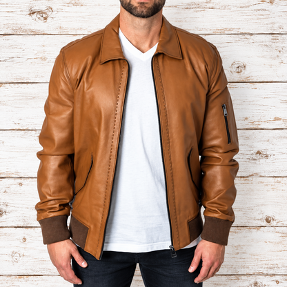 A man wearing a tan leather bomber jacket over a white t-shirt and dark jeans
