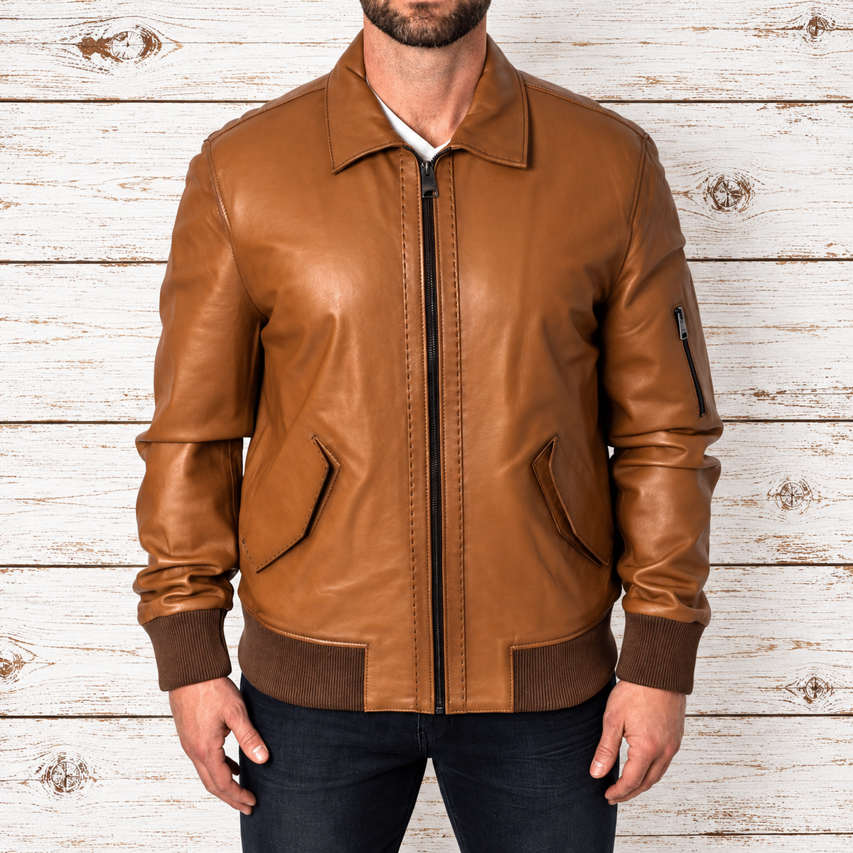 A man wearing a tan leather bomber jacket with dark brown ribbed trim, shown from the chin down 