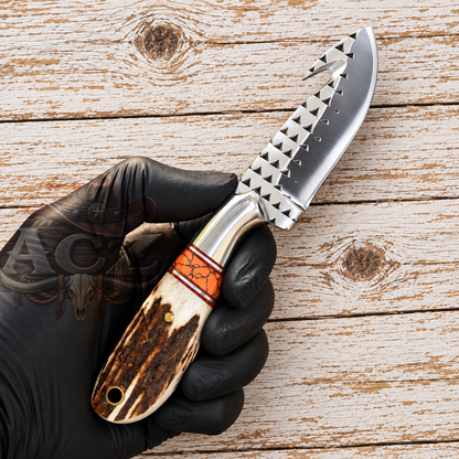 A hand wearing a black glove holds a custom knife with a silver serrated blade and a brown and orange inlay handle, set against a rustic wooden plank background.