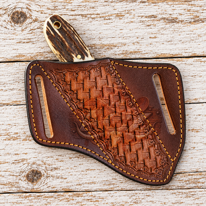 A hand-tooled brown leather knife sheath with a carved wooden handle, displayed on a rustic white-washed wooden plank background.