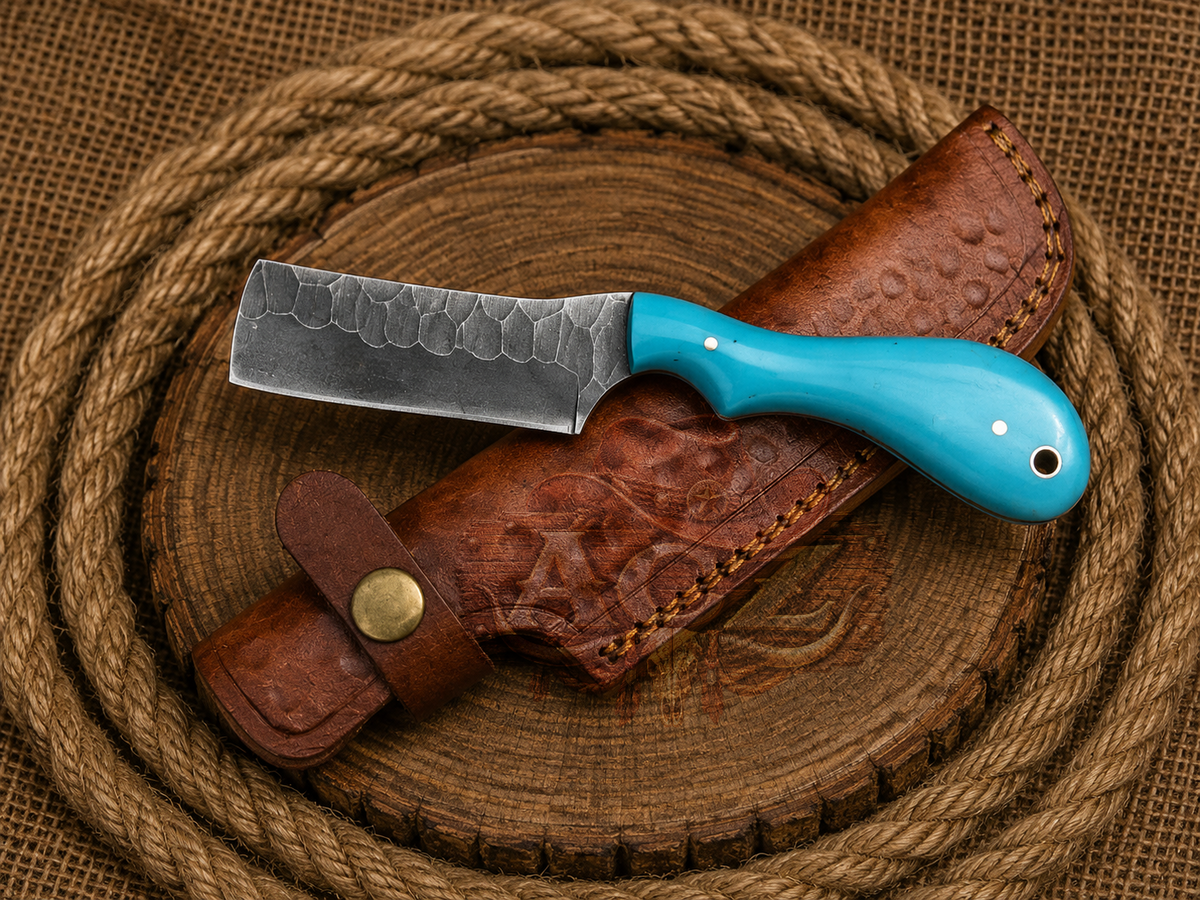 A fixed-blade knife with a hammered dark steel blade and a bright turquoise handle, resting diagonally on a brown leather sheath over a round wooden slice, with coiled rope in the background.
