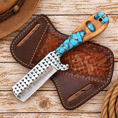 A handcrafted fixed-blade knife with a patterned silver blade, turquoise and wood handle, displayed on a brown embossed leather sheath over a rustic wood plank background.