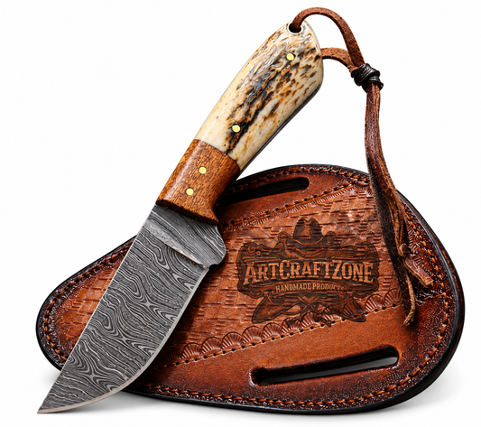 A fixed-blade knife with a patterned Damascus steel blade, a natural horn handle, and a brown leather sheath engraved with the ArtCraftZone logo, shown on a white background.