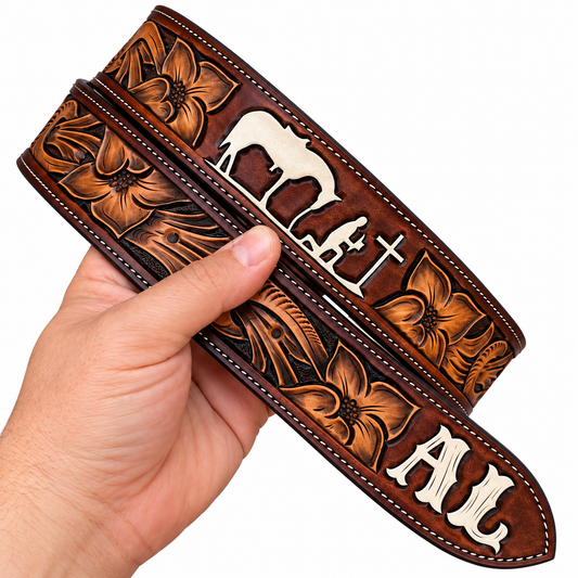 A hand holding a brown tooled leather belt with floral and cross designs, featuring silver-tone metal lettering that reads 'AL'.