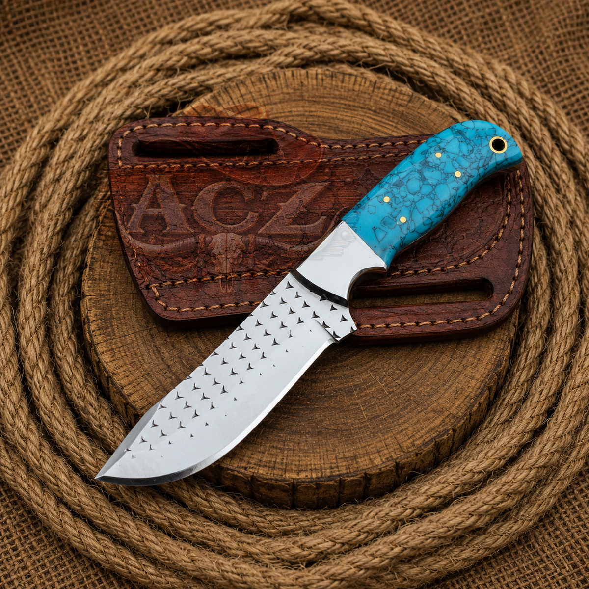 A fixed-blade knife with a silver studded blade and a turquoise marbled handle, resting on a brown leather sheath over a rustic wooden slice and coiled rope background.