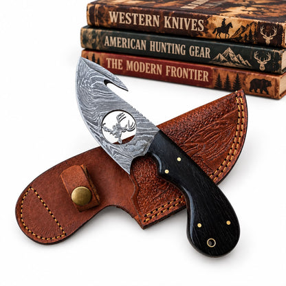 A fixed-blade knife with a patterned steel blade and black handle, displayed in front of a brown leather sheath on a white background, with three stacked western-themed books in the background.