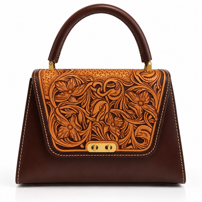 A structured dark brown leather handbag with an intricate floral tooled leather panel on the front flap, featuring gold-tone hardware and a top handle, set against a plain white background.