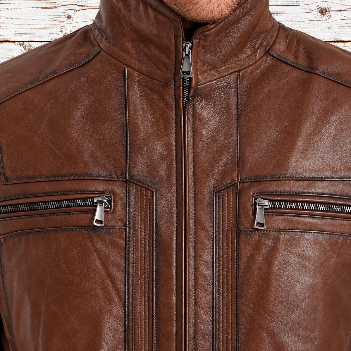 Close-up of a brown leather jacket with a stand collar, center zipper, and two zippered chest pockets