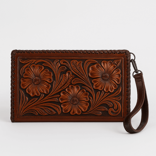 A brown leather wristlet clutch featuring hand-tooled floral designs and braided leather trim, shown with its wrist strap on a light gray background.