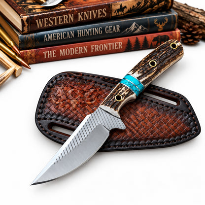 A fixed-blade knife with a textured silver blade and a carved wood handle with a turquoise accent band, resting on a brown woven leather sheath. In the background, stacked engraved books titled 'Western Knives', 'American Hunting Gear', and 'The Modern Frontier' are partially visible alongside bullets and pinecones on a white surface.