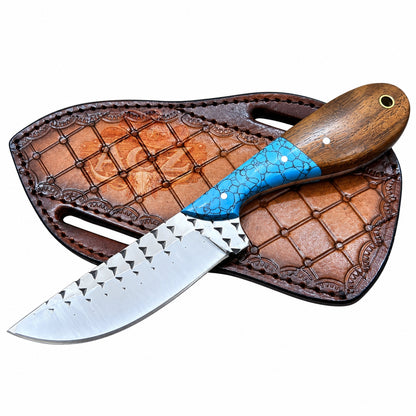 A fixed-blade knife with a silver patterned blade, a brown wood handle, and a textured blue inlay, resting diagonally on its brown leather sheath against a white background.
