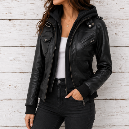 A woman wearing a black leather jacket with a hood, zippered front, and silver hardware, styled with a white tank top and black jeans 