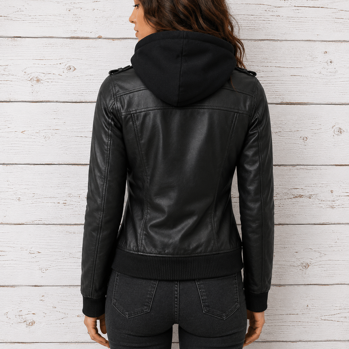 A woman viewed from the back wearing a black leather hooded jacket with ribbed hem and cuffs, paired with dark gray jeans