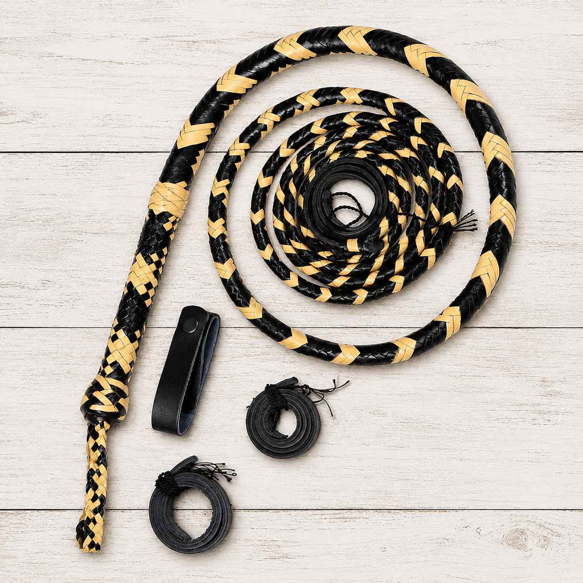A coiled black and tan braided rope with three black accessories laid out on a light wood plank background.