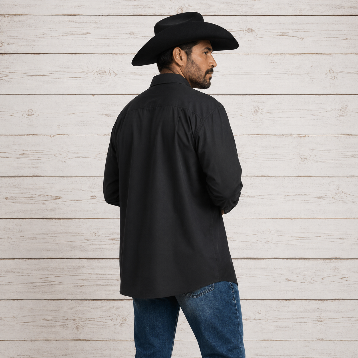 A man wearing a black long-sleeve button-up shirt, blue jeans, and a black cowboy hat, shown from the back and side 